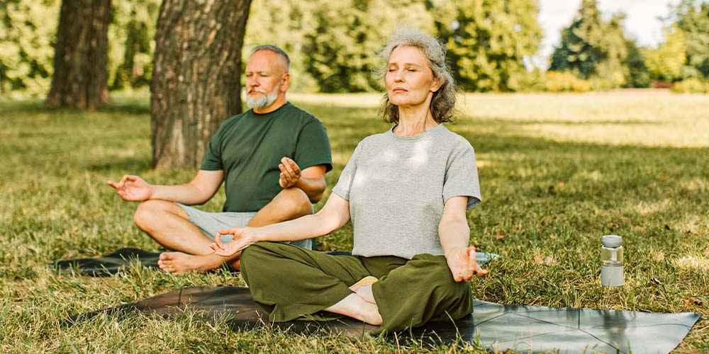 casal de idosos meditando em parque